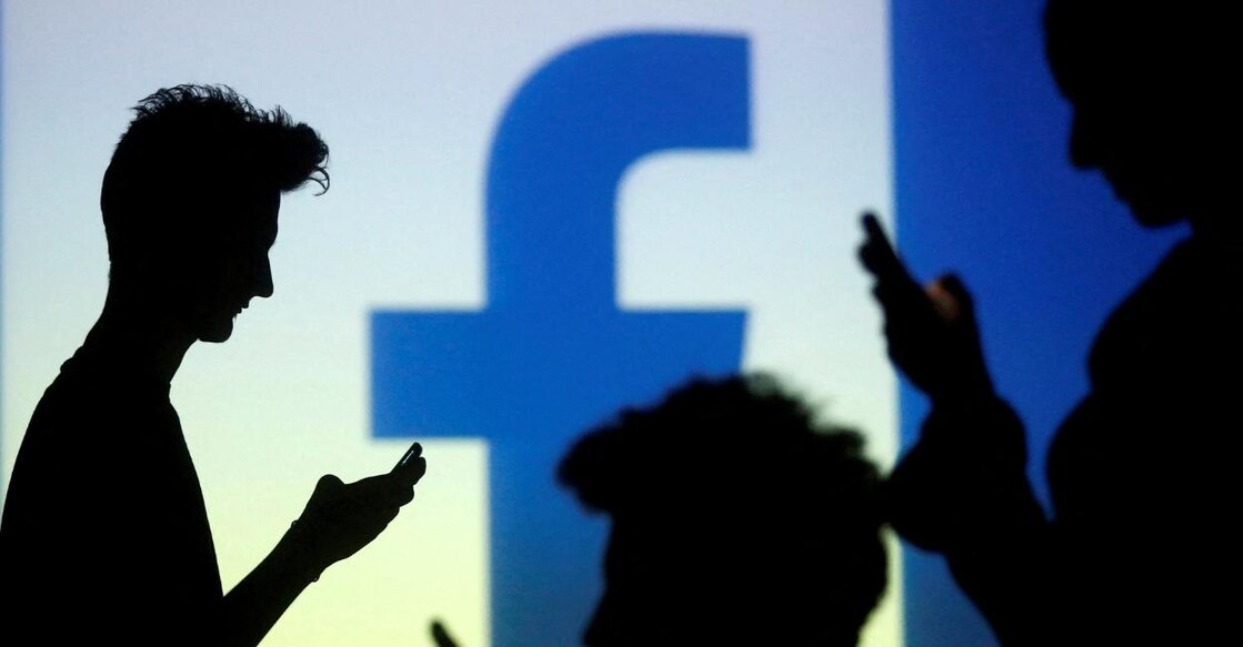 People are silhouetted as they pose with mobile devices in front of a screen projected with a Facebook logo, in this picture illustration taken in Zenica, October 29, 2014. File Photo: Reuters