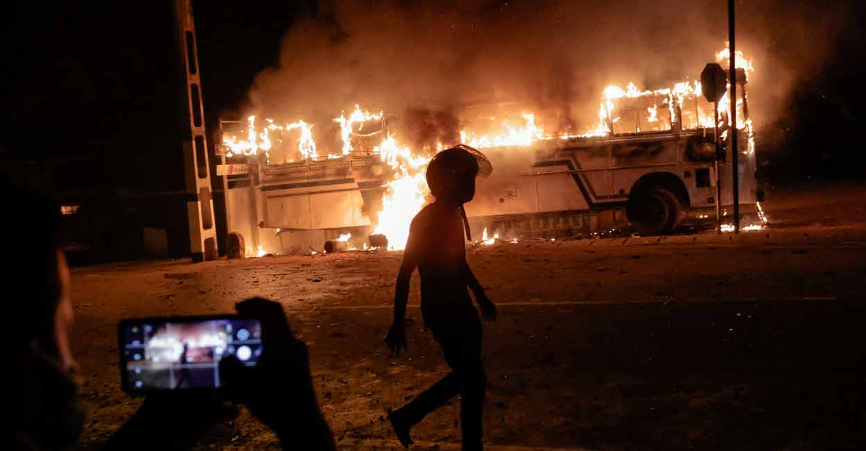 SRI-LANKA-CRISIS A person takes a photo as a demonstrator walks near a bus that was set on fire at the top of the road to Sri Lankan President Gotabaya Rajapaksa's residence during a protest against him as many parts of the crisis-hit country faced up to 13 hours without electricity due to a shortage of foreign currency to import fuel, in Colombo, Sri Lanka March 31, 2022. REUTERS/Dinuka Liyanawatte