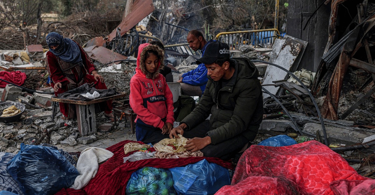 PALESTINIAN-ISRAEL-CONFLICT Palestinians eat outside amid the destruction caused by Israeli strikes in the village of Khuzaa, east of Khan Yunis near the border fence between Israel and the southern Gaza Strip on November 27, 2023. Photo: AFP/ Said Khatib