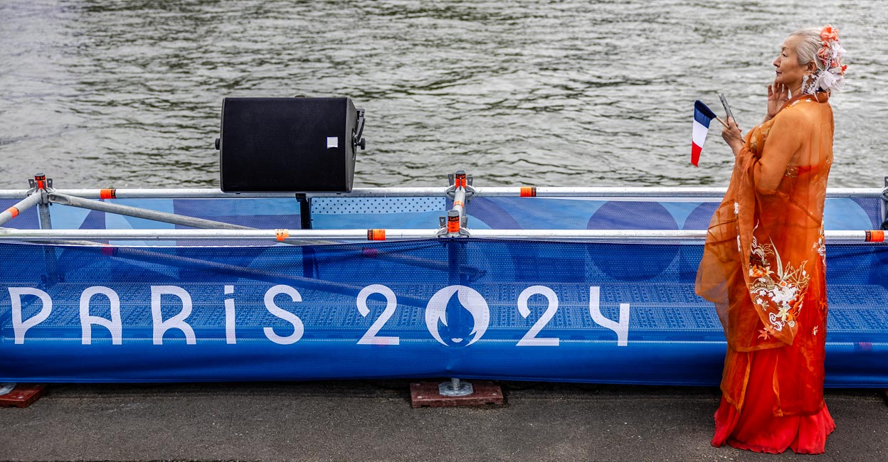 Paris Olympics opening ceremony A woman wearing a traditional Chinese dress holds a French flag while looking at the Seine river before attending the opening ceremony. Photo: AFP/Luis Tato